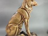 une statue représentant un chien assis sur un socle, à côté d'un ruban