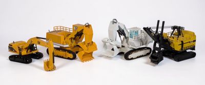 trois engins de chantier miniatures sont alignés sur une surface blanche