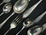 de nombreuses cuillères et fourchettes en argent posées sur une table noire