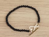 a close up of a black beaded bracelet with a gold arrow charm