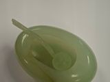 a green bowl with a spoon in it sitting on a table