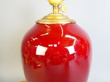 a red vase with a gold lid sitting on a table