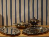 three silver dishes on a table with blue and white striped wallpaper