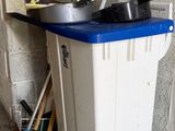 a white trash can with a blue lid and brooms in front of it