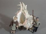 two figurines of people standing in front of a seashell