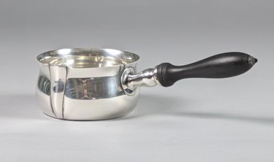 une saucière en argent avec une poignée noire posée sur une table blanche