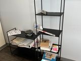 une étagère noire sur laquelle sont posés des livres, dans un coin de la pièce