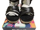 une paire de sandales noires et blanches posées sur une boîte, sur une surface blanche