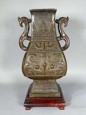 a bronze vase that is on a wooden stand