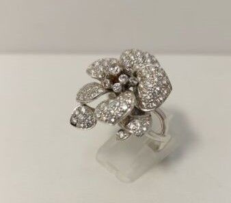 un gros plan d'une bague ornée d'une fleur en diamant posée sur une surface blanche