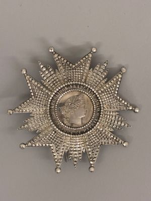 an antique silver sunburst with a coin in the middle of it