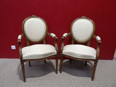 two white chairs with gold trim and white cushions against a red wall