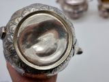 someone is holding a silver tea pot in their hand on a table