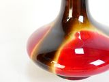 un vase rouge et marron posé sur une surface blanche