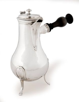 une cafetière en argent avec une poignée noire, posée sur un socle