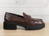 des mocassins en cuir marron à croix, avec des semelles noires, posés sur une table en bois
