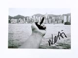 signed photograph of a hand holding up a peace sign in front of a cityscape