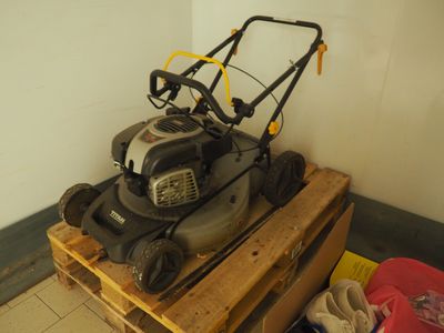 une tondeuse à gazon posée sur une palette dans un coin de la pièce