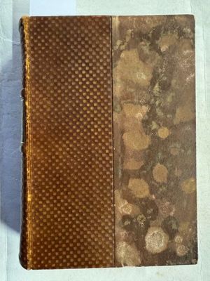 un vieux livre à la couverture marron posé sur une table blanche