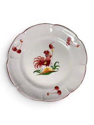 une assiette blanche sur laquelle est représenté un coq, avec des cerises à côté