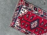 a red and blue rug on the floor next to a black and white cat