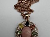 a close up of a necklace with a pink stone surrounded by multi colored stones