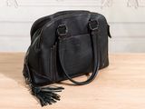 black leather handbag with tassels on wooden table in front of wall