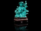 une statuette en jade vert représentant une femme tenant un panier de fleurs, assise sur un rocher