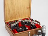 une boîte en bois remplie d'appareils photo et d'autres objets, posée sur une surface blanche