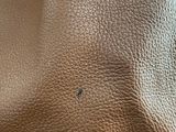 a close up of a tan leather bag with a small hole in the middle