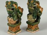 paire de statuettes « foo foo foo » vernissées de vert, posées sur des socles, sur fond gris
