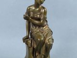 an antique bronze statue of a woman sitting on a rock