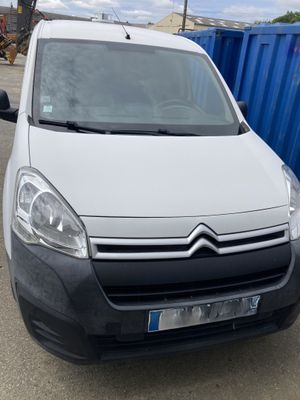 La camionnette blanche est garée sur un parking, à côté d'une benne bleue.