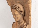wooden sculpture of a woman with a hat on her head hanging on a wall