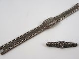 une image représentant une montre en argent et un bracelet en argent posés sur une surface blanche