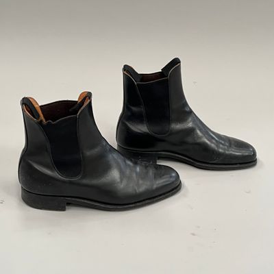 une paire de bottines Chelsea en cuir noir posées sur une surface blanche