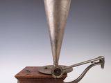 un vieux gramophone plaqué argent posé sur un socle en bois, avec un fond noir