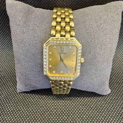 un gros plan d'une montre en or posée sur un coussin, sur une chaise