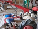 un petit tracteur rouge auquel est attelée une charrue rouge