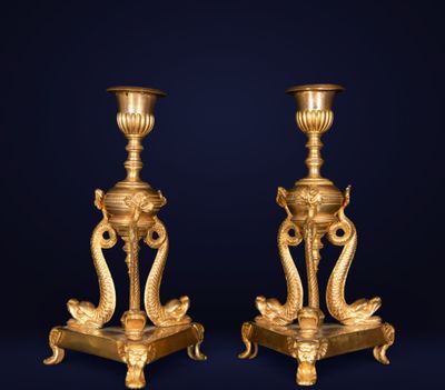 a pair of antique brass candlesticks on pedestals on a dark background