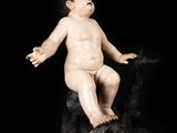 statue of a baby sitting on a rock on a black background