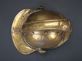 brass helmet mounted on the wall of a room with a black background