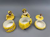 quatre figurines en céramique représentant des femmes vêtues de robes jaunes et coiffées de chapeaux