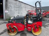 an image of a red and black road roller parked in front of a building