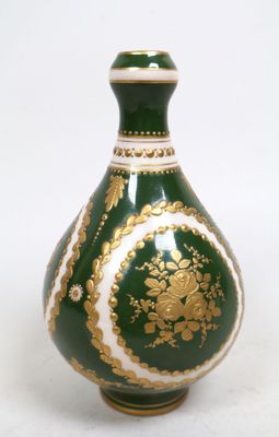 un vase vert et doré posé sur une surface blanche