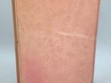 an old book with a pink cover sitting on top of a table