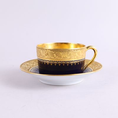 une tasse à café et une soucoupe dorées et noires posées sur une surface blanche