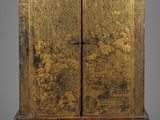 une armoire ancienne en bois dont les portes et les tiroirs sont recouverts de peinture dorée