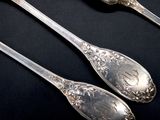 two silver spoons and a fork on a black table