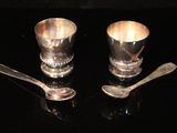 two silver cups and spoons sitting on a table